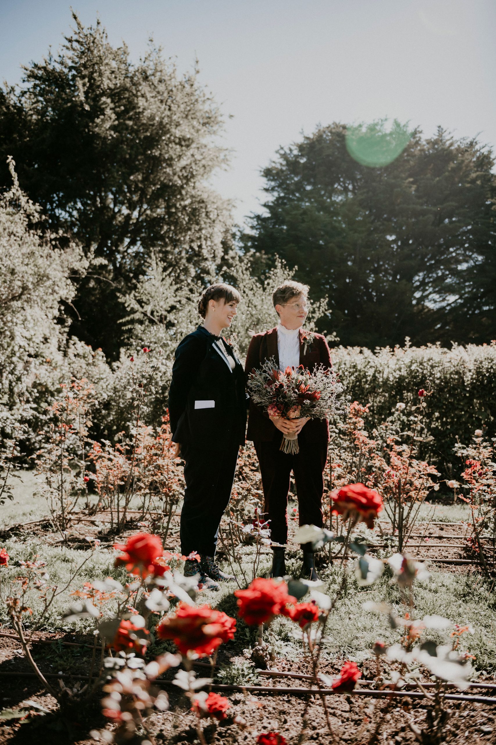 Couple stands sun drenched amongst roses during ceremony at rose farm Acre of Roses Elopement Lets Elope Melbourne Celebrant Photographer Elopement Package Victoria Sarah Matler Photography Acre of Roses Trentham intimate weddings