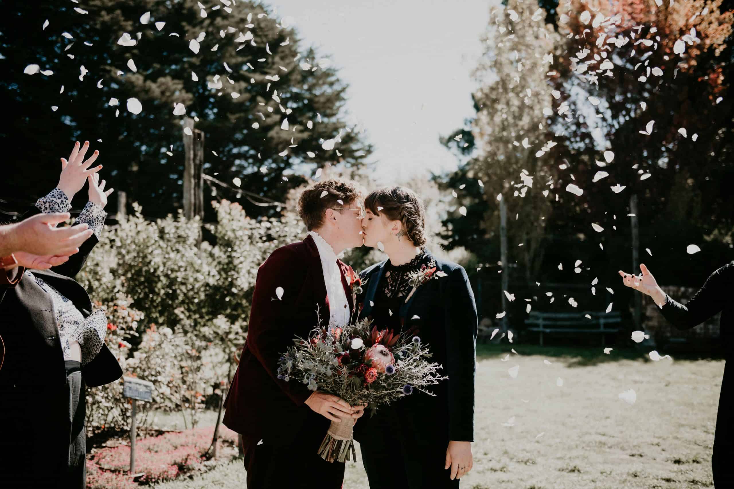 Couple kiss under rose petals thrown in the air. Let's Elope Melbourne professional elopement packages for a small intimate wedding. Beautiful ceremony and photography elopement packages