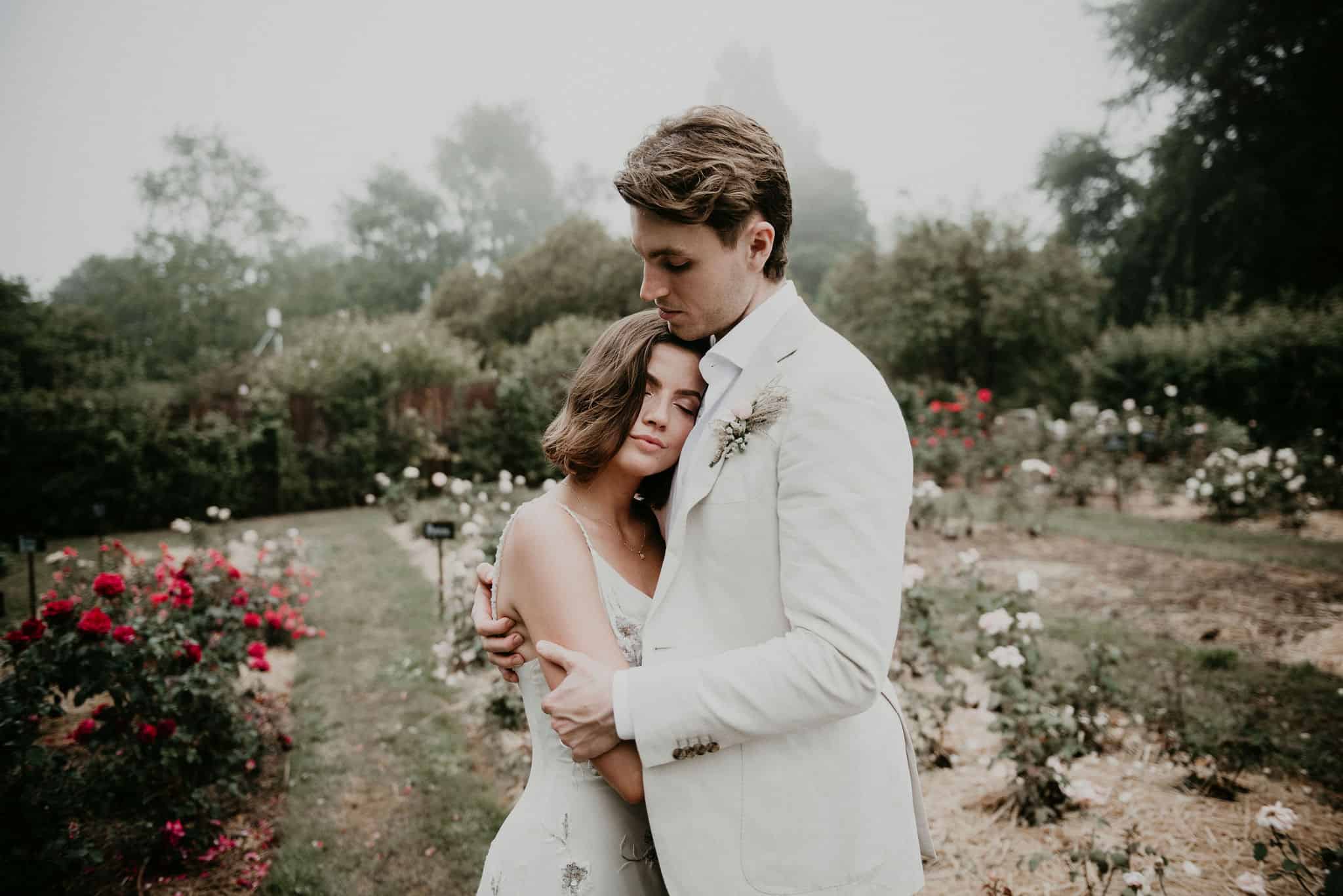 Couple hug in an intimate moment lovingly amongst the roses after beautiful wedding ceremony with Let's Elope Melbourne Celebrant Photography Elopement Package Victoria photographed by Sarah Matler Photography at Acre of Roses Trentham