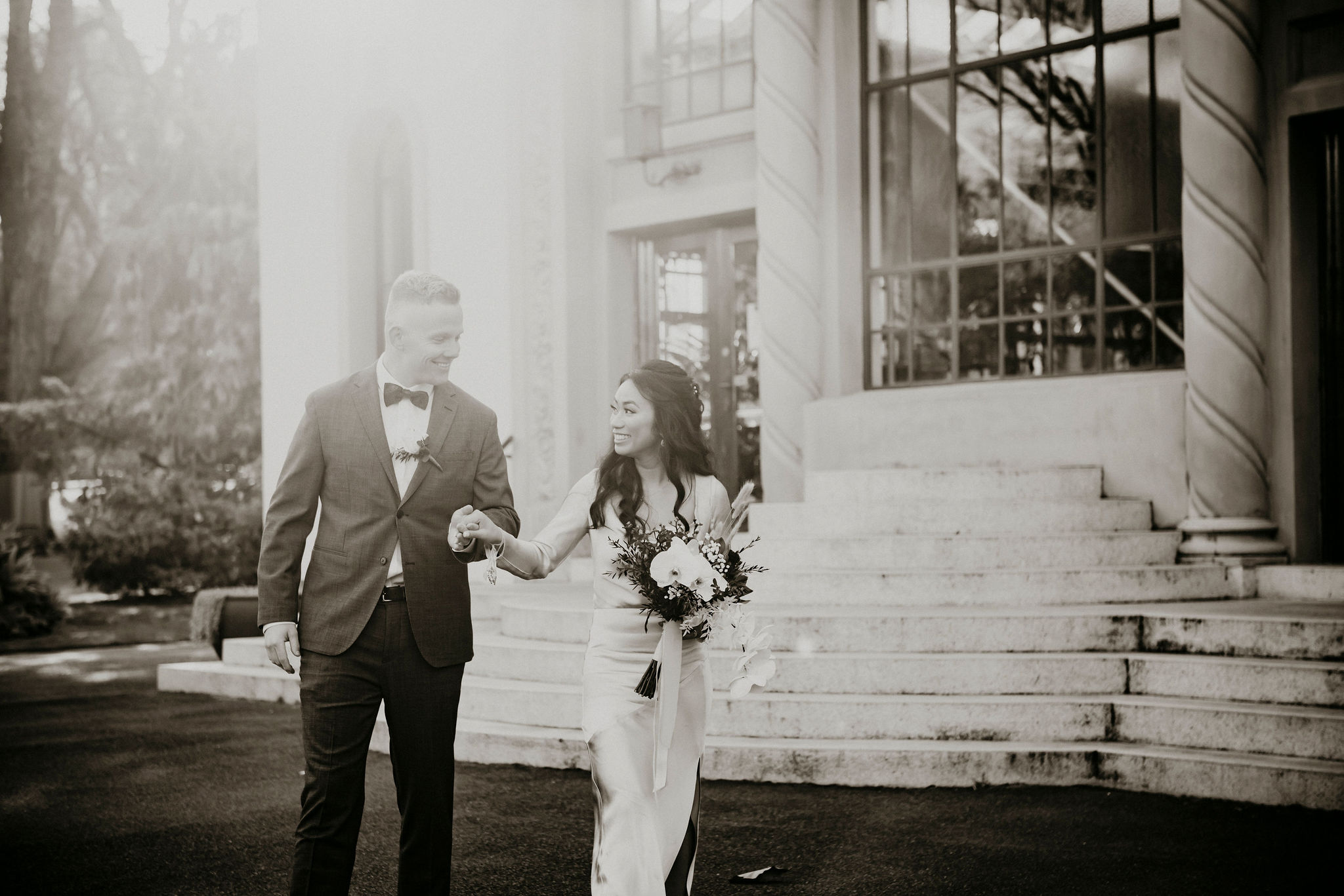 Couple walks holding hand with sun flare in front of conservatory in the Fitzroy Gardens Melbourne Ceremony and Photography - simple yet elegant ceremony which can be personalised and packaged with beautiful photography you will cherish forever Lets Elope Melbourne Celebrant Photographer Elopement Packages Victoria Sarah Matler City Wedding Photos