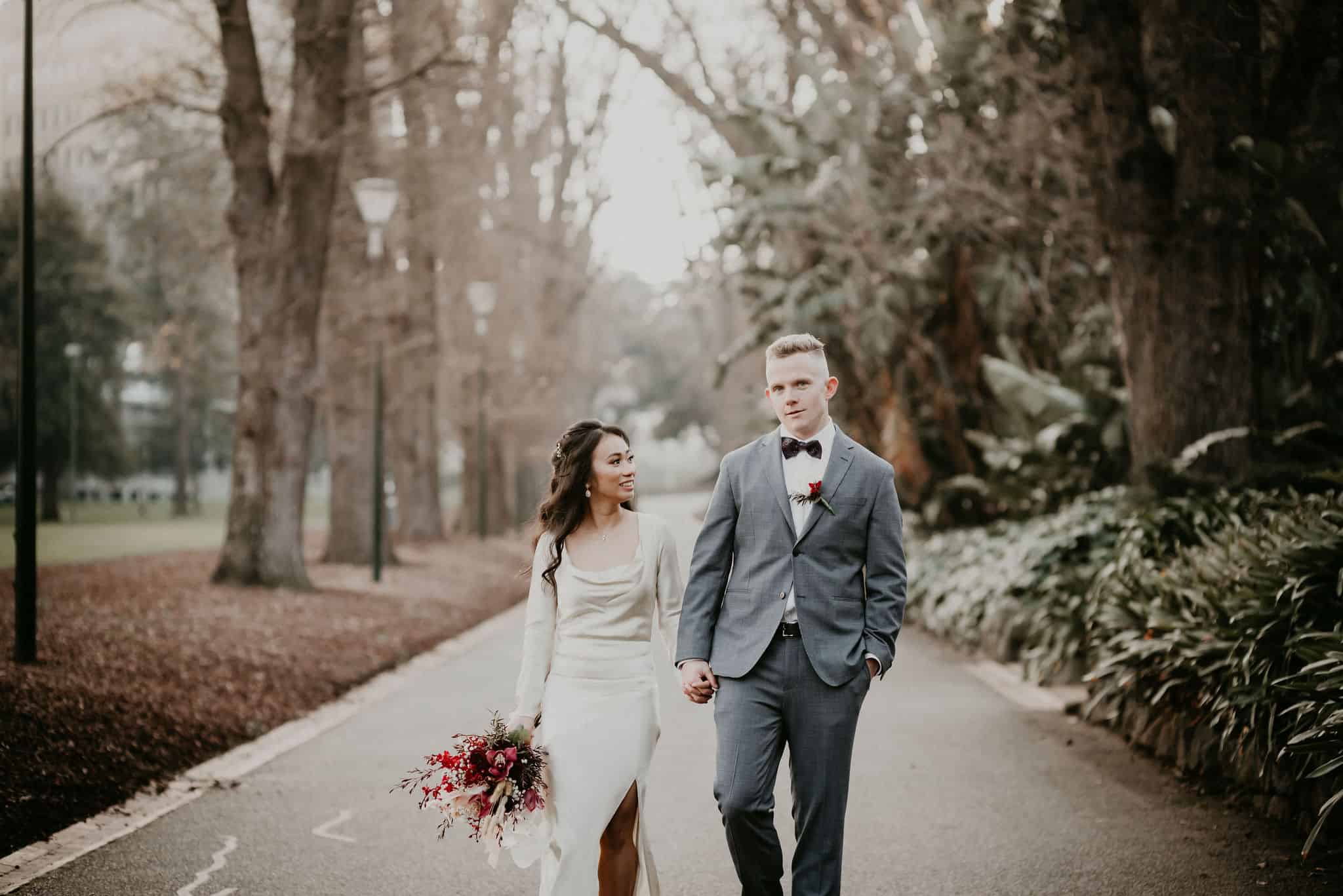 Bride and groom walking through park on a winters day after beautiful ceremony with Let's Elope Melbourne celebrant photography elopement package Victoria Sarah Matler Photography Fitzroy Gardens city wedding photos