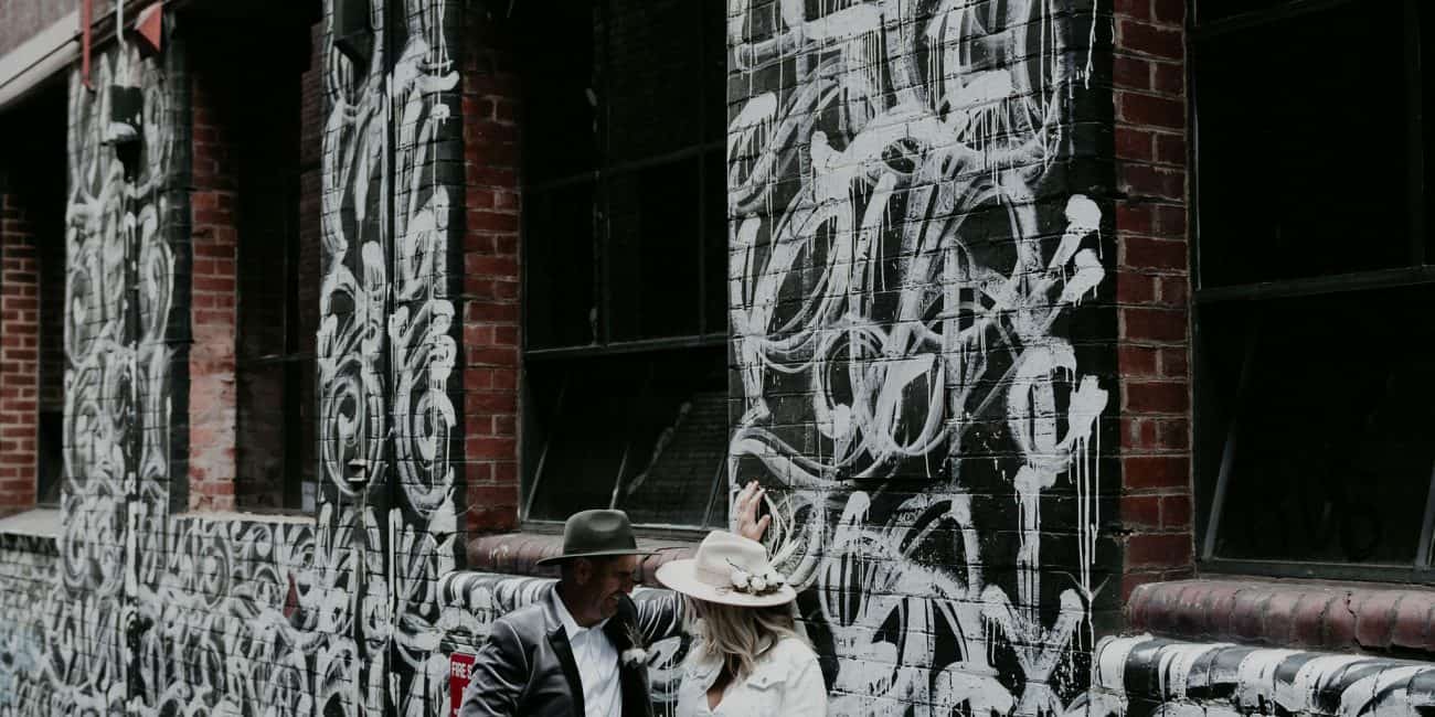 bride and groom leans agains graffiti wall laughing candid Let's Elope Melbourne celebrant photography elopement package Victoria Sarah Matler Photography Fitzroy Gardens city wedding photos ACDC Lane laneways alternative wedding ceremony