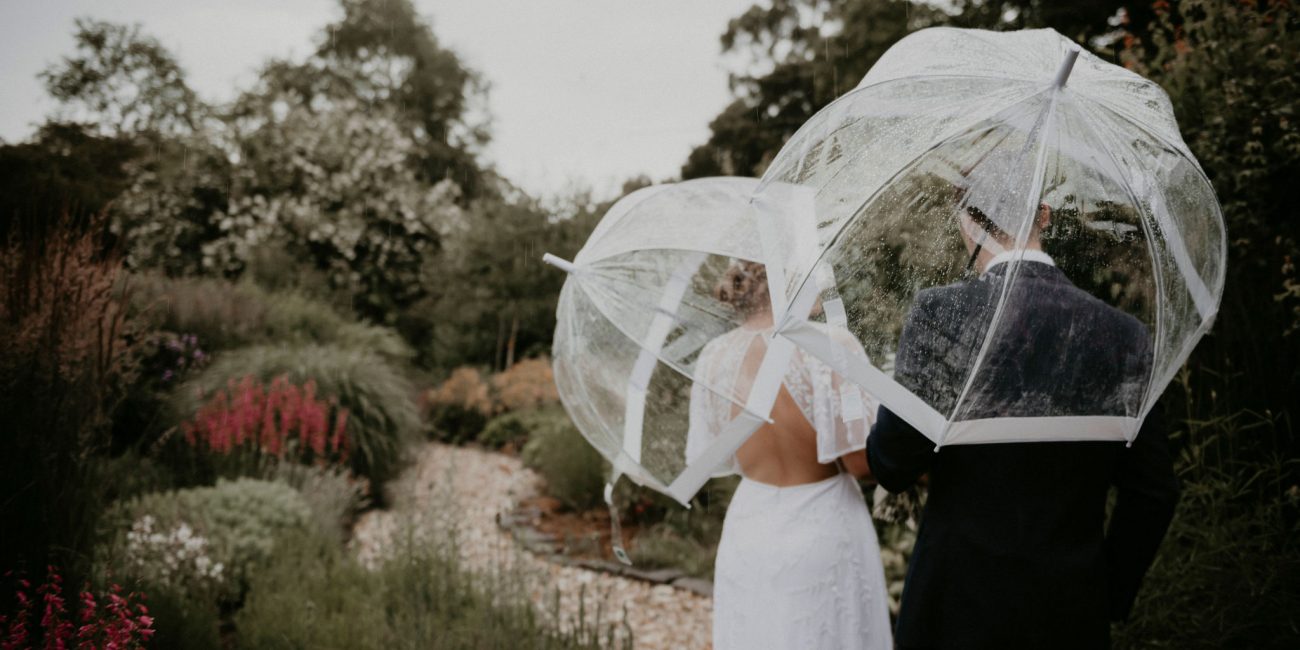 Couple walks through garden with umbrellas in the rain Rose Farm Elopement Videography