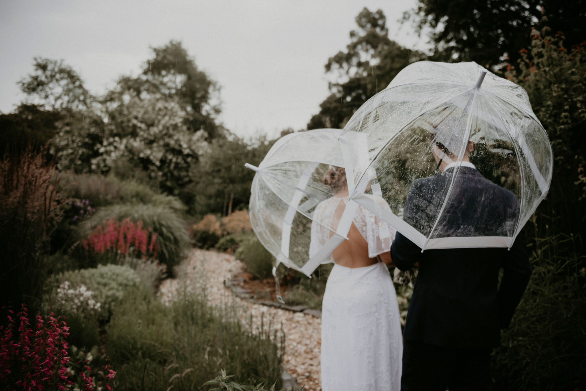 Couple walks through garden with umbrellas in the rain Rose Farm Elopement Videography
