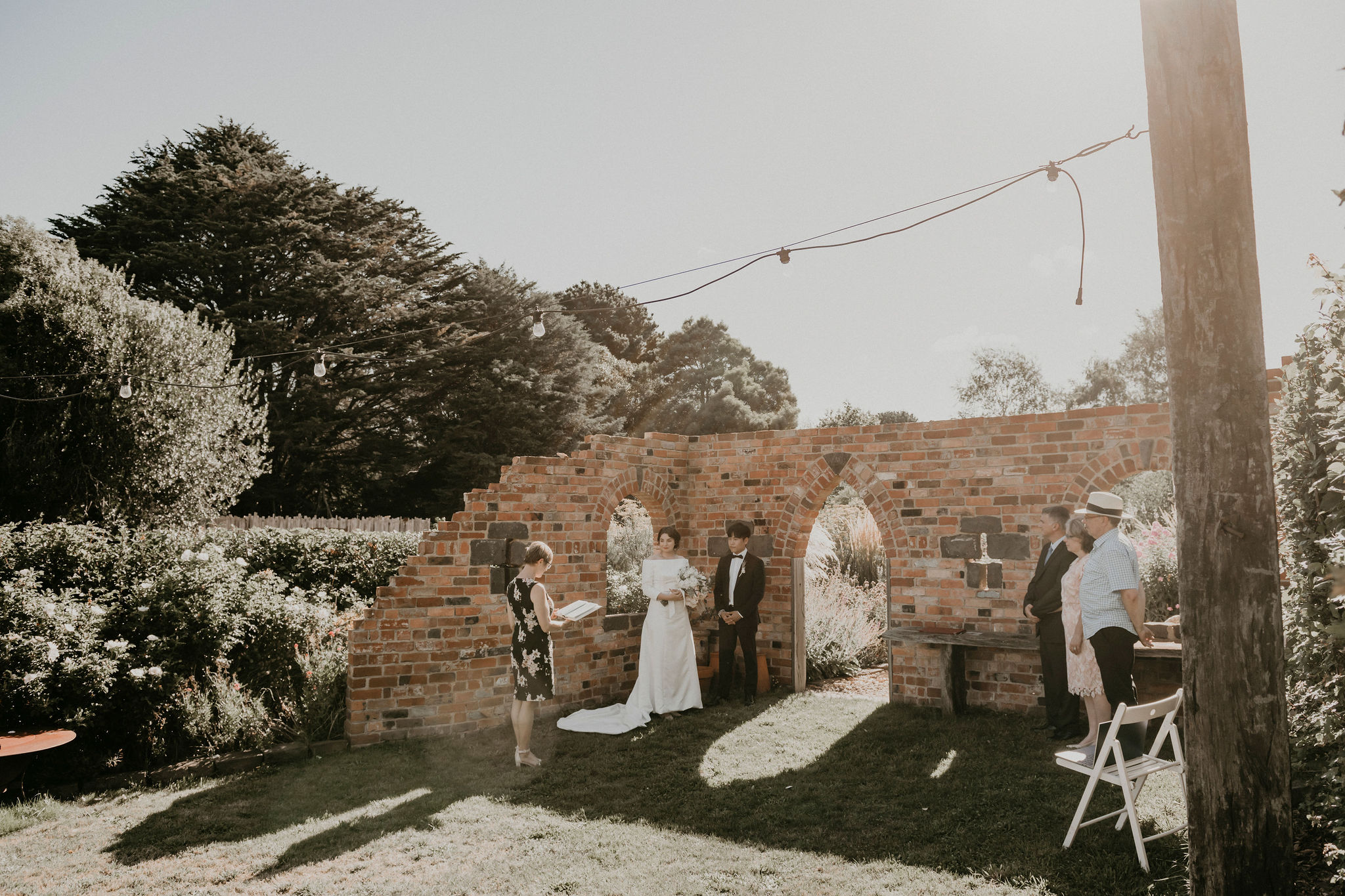 Ceremony takes place by the brick folly bathed in afternoon sunlight with close family Let's Elope Melbourne Portfolio Celebrant Photographer Elopement Packages Victoria Sarah Matler Photography intimate weddings Acre of Roses Trentham romantic ceremony