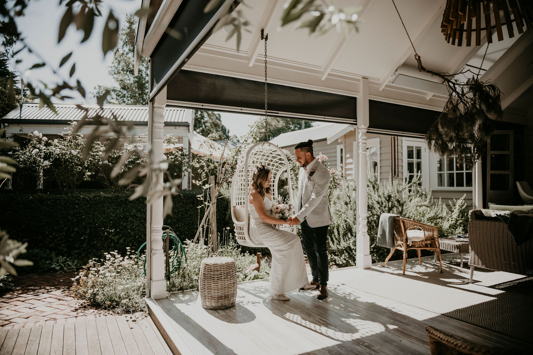 Bride sits in hanging chair on patio while groom stands holding her hand Let's Elope Melbourne Portfolio Celebrant Photographer Elopement Packages Victoria Sarah Matler Photography intimate weddings Acre of Roses Trentham romantic ceremony