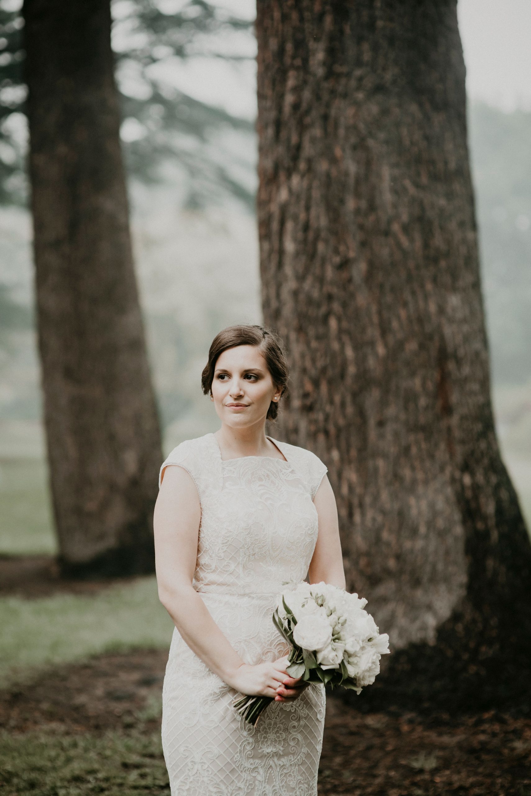 Bride stands in front of tree line in the rain and fog Let's Elope Melbourne Portfolio Celebrant Photographer Elopement Package Victoria Sarah Matler Photography intimate wedding Fitzroy Gardens Foggy Moody East Melbourne
